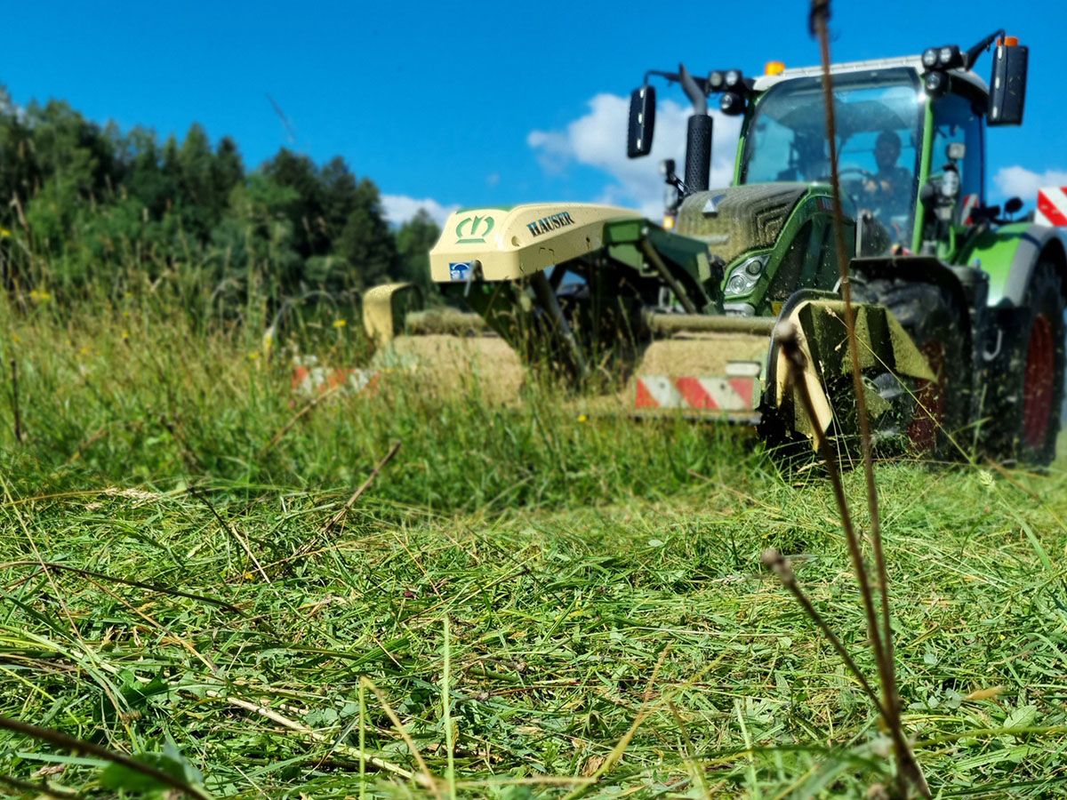 Traktor mäht hohe Wiese unter blauem Himmel für frisches Futtergras